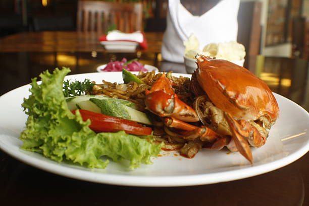 Savor a plate of delicious fried noodles with a whole cooked crab, fresh green lettuce, cucumber slices, and a lime wedge at a restaurant A vibrant and appetizing meal ready to be enjoyed