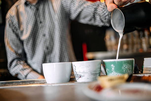 Man working at bar and adding milk on top of espresso coffee on bar counter