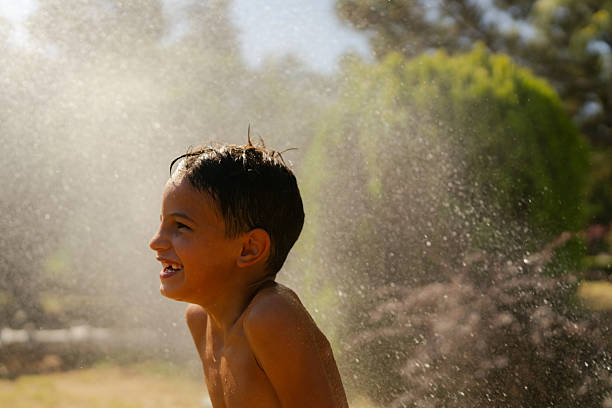 Happy Kid chasing and playing with soap bubbles in garden, Funny Child catching and bursting bubbles outside in summer. Young Boy having fun on weekend, Outdoor activity for Children concept