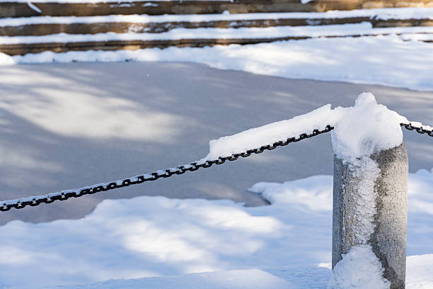 Black metal chain partially covered in snow frames a frozen surface with snowy steps in a quiet winter landscape