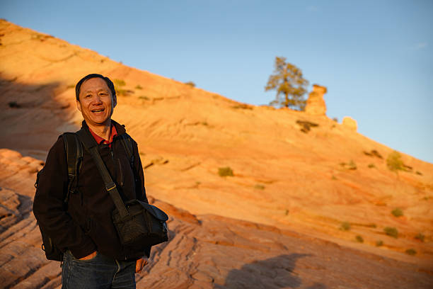 Backpacker stands on the rocks and smiling. The setting Sun casts a golden glow on the rocks. Zion National Park. Utah. USA.