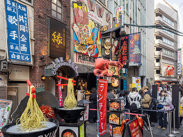 Osaka, Japan - December 08, 2025: Dotonbori's vibrant street scene with a lively crowd, illuminated restaurant signs, and unique food displays, including a prominent ramen noodle sculpture and an