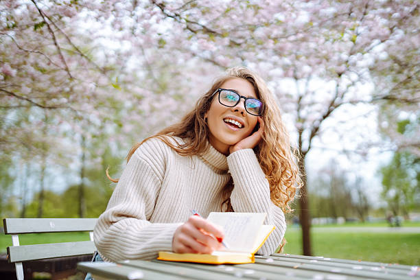 Young man surprising his girlfriend with a beautiful bouquet of flowers while she is relaxing on the sofa, reading a book, in their modern apartment