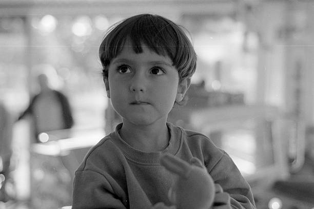 Little boy is looking up with curiosity, holding a small toy while experiencing childhood moments. Black and white background. Scanned from analog film