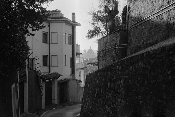 Winding alley leading towards buildings and a distant view of the Duomo dome in Florence, Italy, shot in black and white film. Scanned from analog film