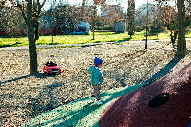 Little boy in hat and yellow jacket plays in a garden