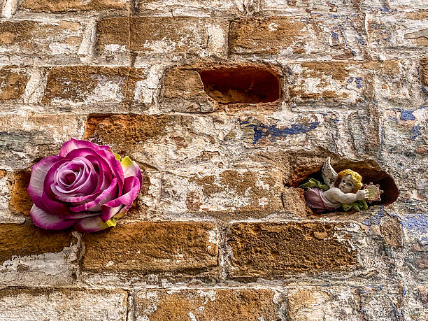 Low angle close-up view of a rose and a small angel figurine embedded in an old brick wall