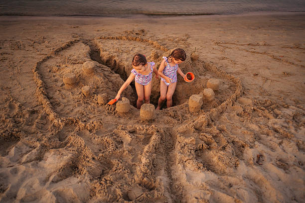 Young girls building sandcastle on beach by ocean