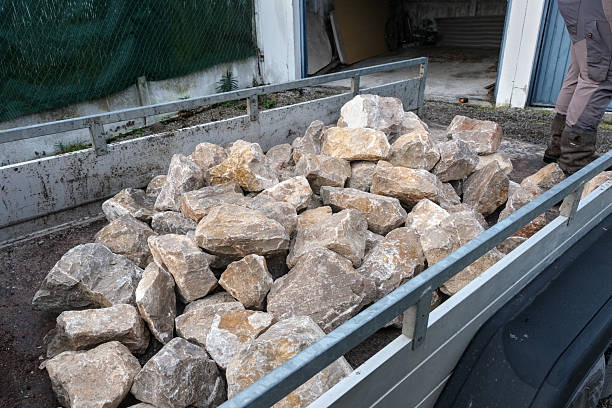 Rough stone loaded in a metal trailer at a construction site, showing natural rock texture, manual labor, and outdoor building materials.