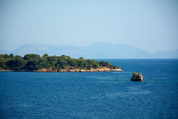 Peaceful Mediterranean seascape with small pine covered island, deep blue water and distant hazy mountains, expressing tranquility, escape, summer travel and natural beauty for premium design use