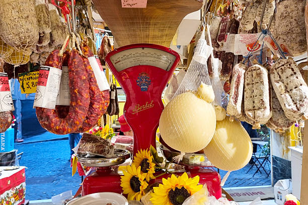 Rome, Italy, December 29, 2025: Vibrant italian market scene showcasing an array of cured meats and cheeses hanging above a vintage red scale. sunflowers adorn the display, adding a touch of color and charm to the authentic market setting.
