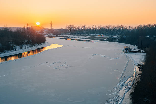 Ice on the shore of lake. Sky with pink clouds reflected in the cold water at sunset. Abstract winter nature background