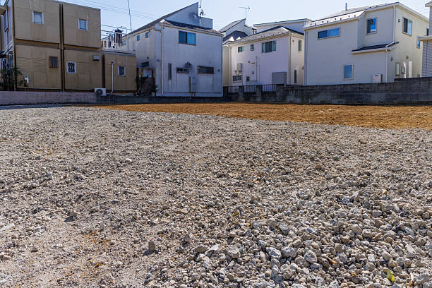 A neatly leveled vacant lot in a quiet residential area. A construction site covered with gravel and soil, marked off with ropes. Image of real estate and land utilization.