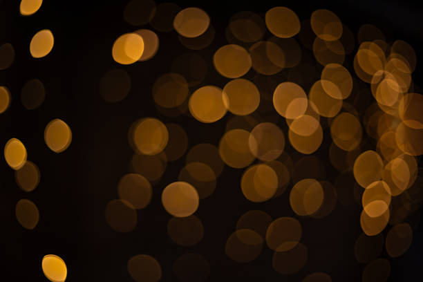 Golden bokeh circular lights glowing on a dark abstract background creating a warm atmosphere