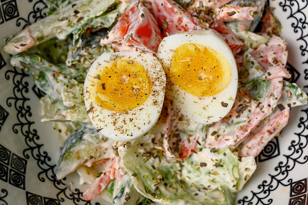 Vegetable salad with mayonnaise dressing and a boiled egg in a deep ceramic bowl. A serving of fresh salad with tomatoes, cucumbers and herbs garnished with egg halves on a plate