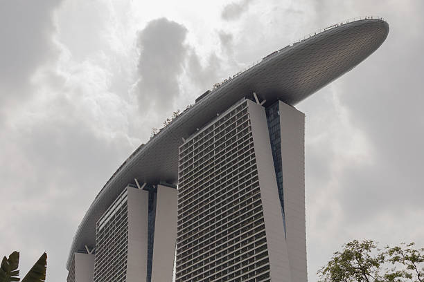 Singapore - January 27, 2026: Tall buildings make up Marina Bay Sands in Singapore. The structure has a unique design with an oval roof. Bright skies are filled with clouds. People walk nearby.