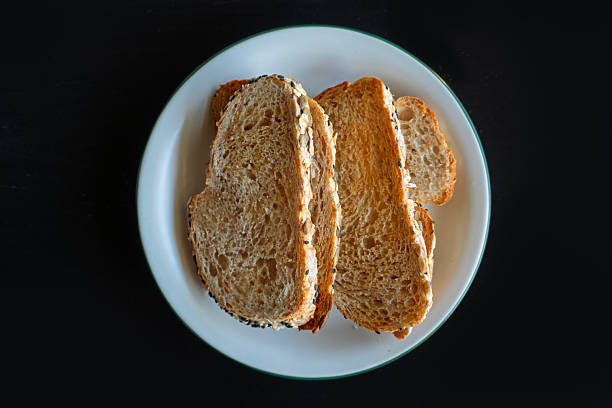 Top view of sliced whole grain bread arranged on a white plate over a black background.