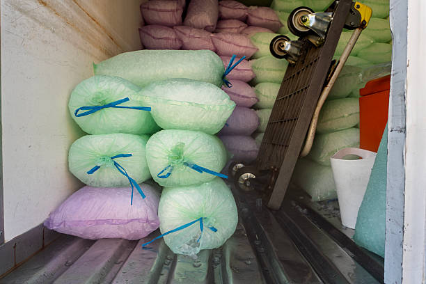Stacks of bagged ice stored inside a refrigerated truck compartment, with plastic-wrapped ice packs arranged on the metal floor alongside a hand truck.