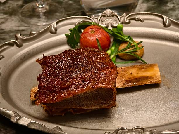 Roasted meat with bone on a decorative plate garnished with herbs and tomato