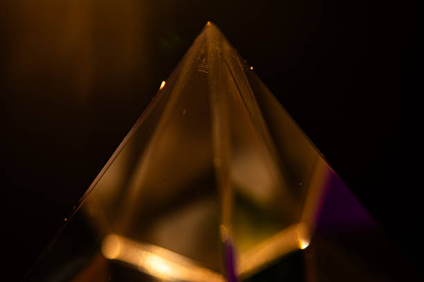 Soft abstract shot of a glass pyramid illuminated by warm golden light on dark background, creating dreamy bokeh and atmospheric glow for creative design projects.