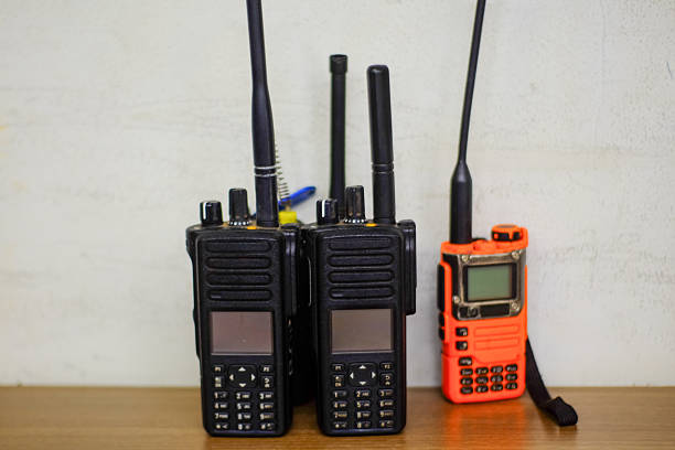 Portable two way radios displayed side by side showcasing modern communication devices Two black and one orange walkie talkie stand ready for use