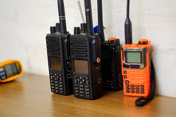Diverse array of professional walkie talkies including black and a bright orange model resting on a polished wooden desk suggesting preparedness and connectivity