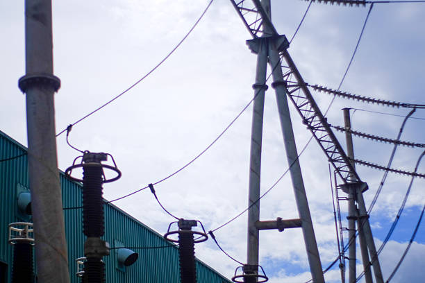 View of an electrical substation showing large gray metal structures power lines and ceramic insulators A corrugated teal building is visible in the background