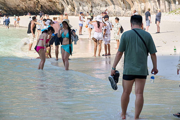 Crowded tropical beach with tourists standing in the shallow water