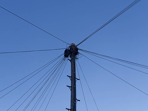 A close-up photograph of utility lines and support towers with mountains in the background
