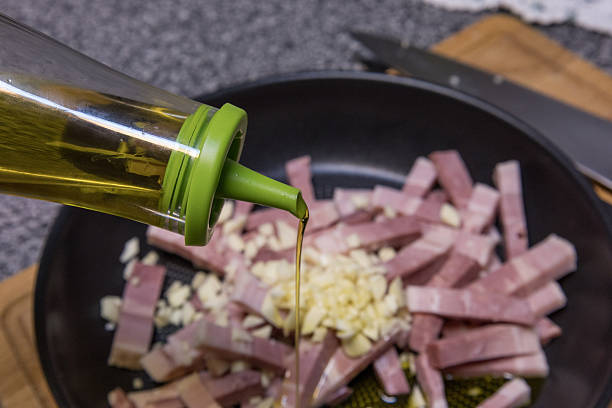Pouring olive oil into a hot skillet with diced bacon and minced garlic for frying