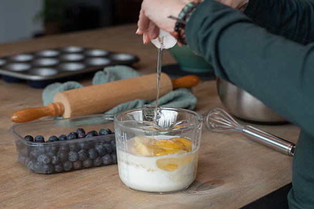 Close-up of hands cracking an egg into a measuring cup as part of homemade muffin baking preparation