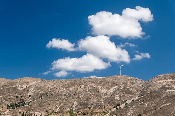 Single wind turbine on a dry mountain ridge under a clear blue sky with white clouds. Renewable energy, sustainable electricity production, green technology and clean energy concept. Minimal landscape with copy space, environmental conservation and climate change solution.