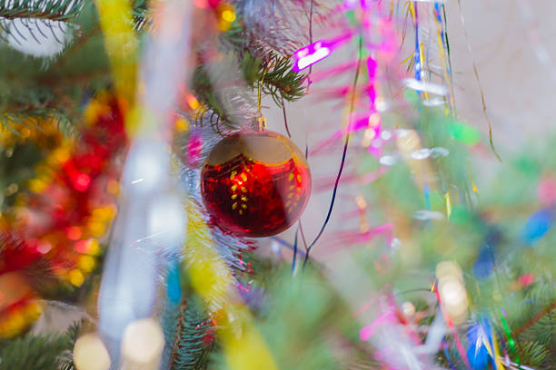 Dreamy blurred background of a Christmas tree with soft focus on a red shiny bauble and shimmering colorful garlands. Artistic holiday concept.