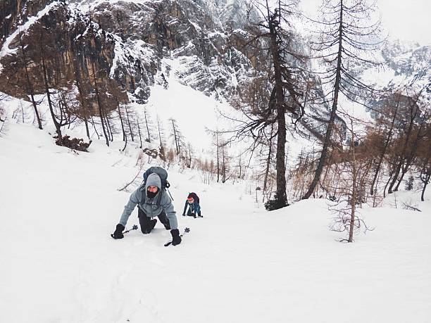 Two climbers ascending a snowy mountain slope, surrounded by rocky terrain and sparse trees, winter adventure