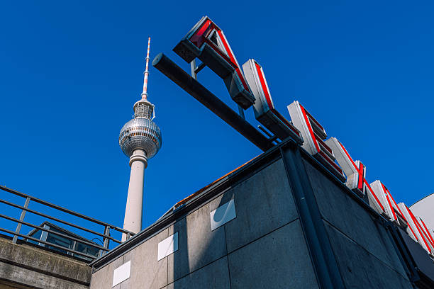Urban Berlin scene featuring the Fernsehturm and bold red-white signage against a clear blue sky. A modern, architectural composition that conveys city energy and iconic landmarks.