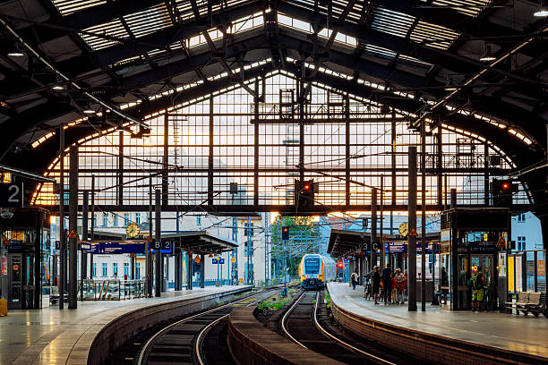Sunset light bathes a Berlin railway station as trains arrive and depart along curved tracks. reflections, glass walls, and motion blur convey urban transit and daily travel.