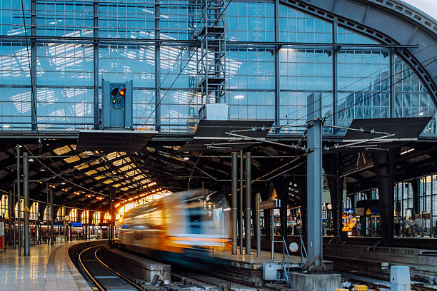 Sunset light bathes a Berlin railway station as trains arrive and depart along curved tracks. reflections, glass walls, and motion blur convey urban transit and daily travel.