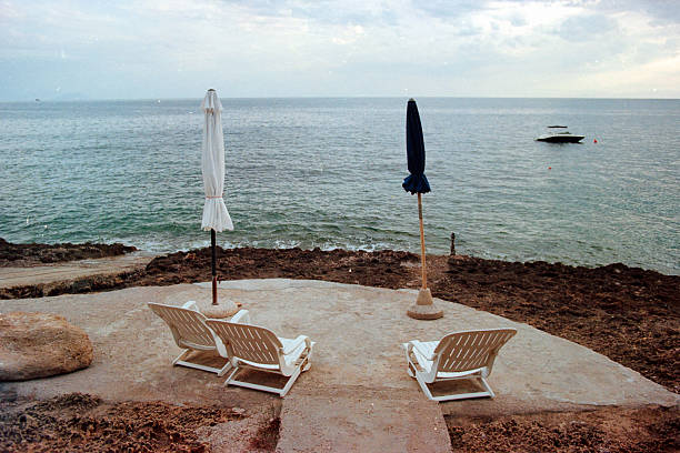 Relaxing by the sea with beach chairs and umbrellas on a coastal terrace, a small boat floating in the distance. Scanned from analog film