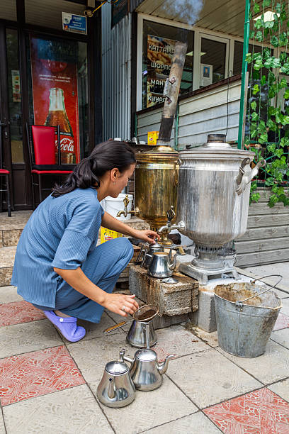Adult asian woman pouring tea from samovar outdoors at roadside teahouse in daylight in Cholok, Kyrgyzstan - July 16, 2024