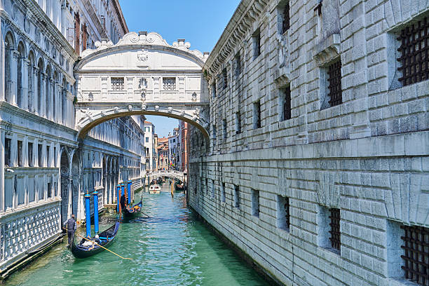 Venice, Italy - February 21, 2022: A Venetian gondolier expertly navigates his gondola and passengers through the narrow canals of Venice, Italy. In this case the gondola has just passed beneath the famous Bridge of Sighs.