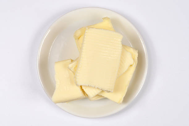 Top view of several rectangular slices of fresh yellow butter stacked on a small white ceramic plate over a white background