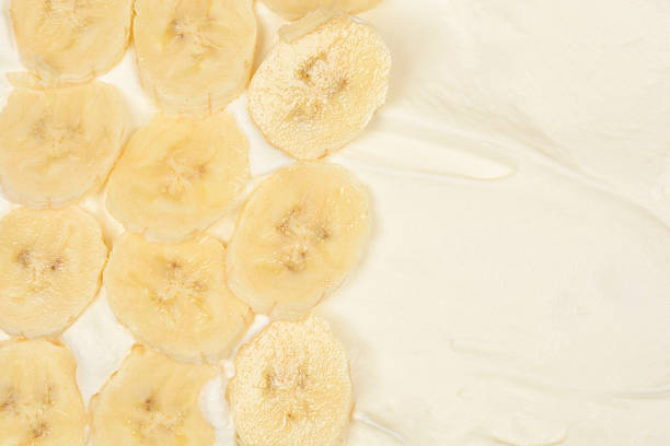A top view close up showing fresh yellow banana slices arranged on a thick layer of smooth white whipped cream