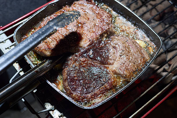 barbecue party, close-up image of grilling steaks, the meat is stewed in butter with garlic and thyme, spiking pieces of meat on the grill, various vegetables, lots of smoke