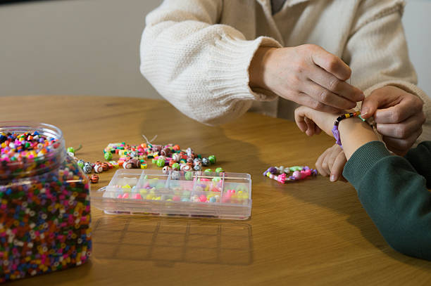 A cozy scene of a mother and her child sitting at a table, surrounded by jars of beads and craft supplies, focusing on a creative task.