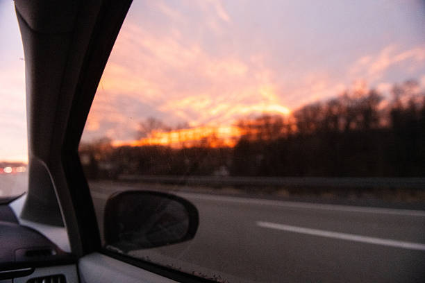 This is a photograph of a sunset sky over the sihouetted highway and bare trees on a West Virginia highway in winter and seen from a car’s passenger side.