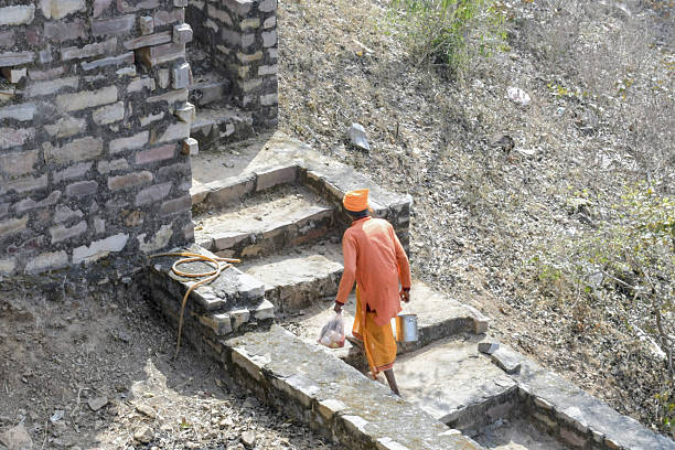 rohotashgarh fort, kaimur hills, bihar, india- january 30, 2026: a priest in traditional orange attire walks up ancient, crumbling stone stairs toward the rear of the chaurasan temple