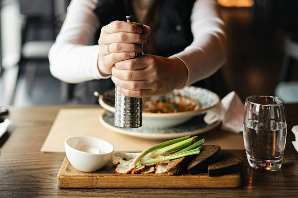 A woman in a restaurant adds pepper or salt to her dish.