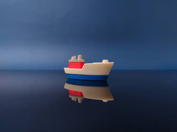 This is a small plastic toy boat, possibly a cargo ship with reflection on a dark blue background.