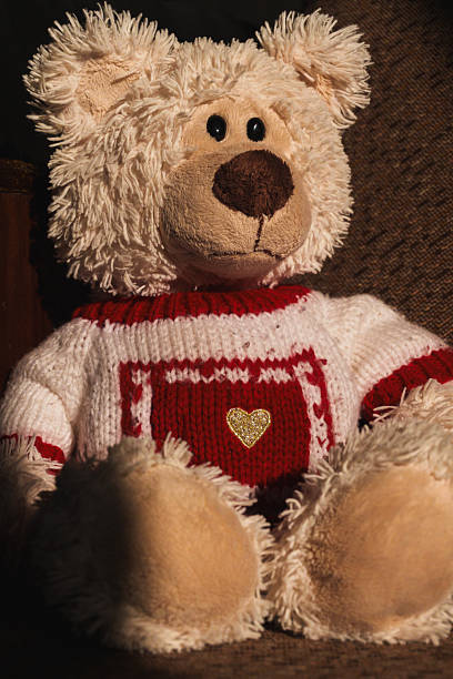 A stuffed teddy bear with a red and white striped sweater on a white background, flay lay, top view. A soft toy against the backdrop of warm summer sunshine. The bear has brown eyes and a brown nose