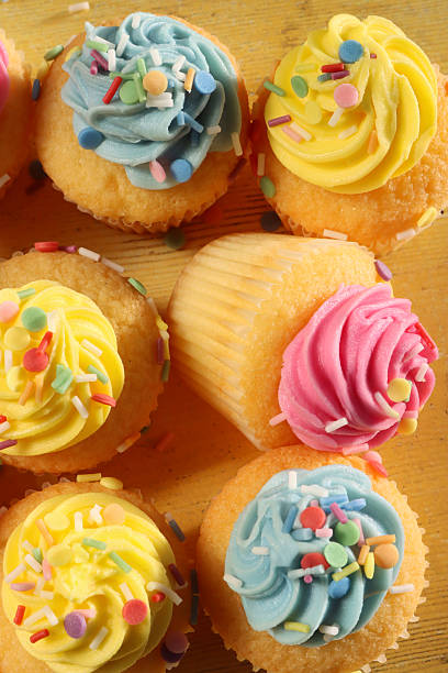 Stock photo shows an overhead composition of homemade Easter cupcakes, cakes, and muffins baked in soft pastel colours of blue, yellow, and pink. Each dessert is topped with creamy butter icing and playful sprinkles, forming a vibrant bakery spread
